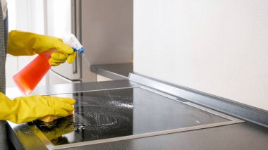 Genç ev hanımı mutfakta elektrikli sobayı temizlerken kimyasal sprey kullanıyor.
