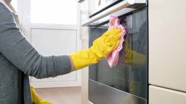 Lastik eldivenli genç bir kadın, mutfağı bez ve deterjanla temizliyor.