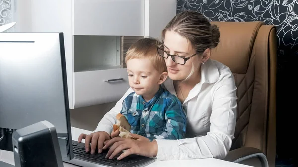 Yung empresária sentada com criança em casa e trabalhando no computador do escritório em casa — Fotografia de Stock