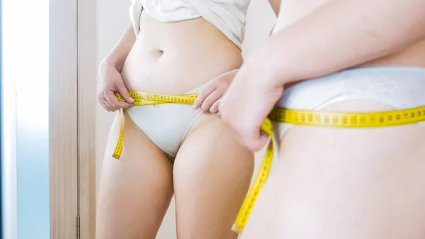 Młoda kobieta stojąca przed lustrem i mierząca talię. Pojęcie nadwagi, odchudzania i diety — Zdjęcie stockowe