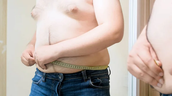 若い脂肪男測定テープで大きな足の腹を測定します。男性の太りすぎ、体重減少と食事療法の概念 — ストック写真