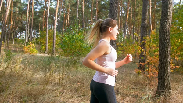 Portrait of smiling young woman with ponytail running in forest — Stock Photo, Image
