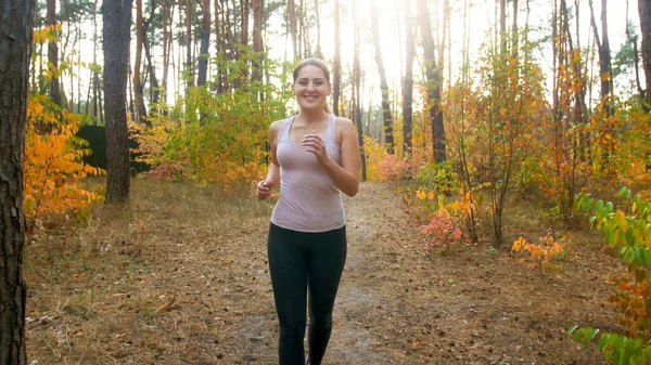 Mutlu gülümseyen genç kadın sonbahar ormanında koşuyor ve spor yapıyor.. — Stok fotoğraf