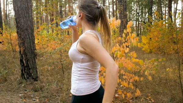 森の中を走る若いブロンドの女性の肖像画とボトルから水を飲む. — ストック写真