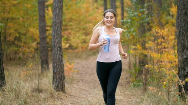 Portrait of young smiling woman jogging and holding bottle of water — Stock Photo, Image