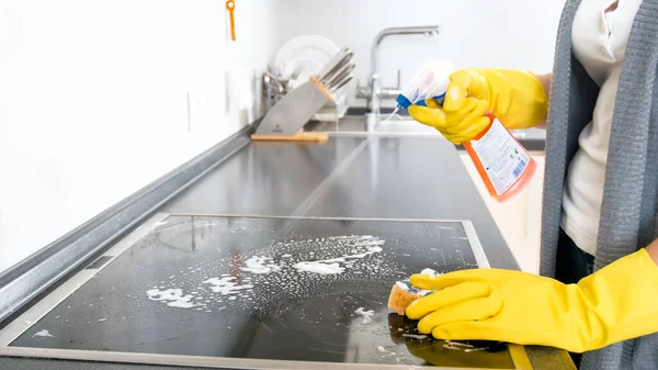 Ama de casa joven usando aerosol detergente para limpiar la cocina eléctrica de vidrio en la cocina — Foto de Stock