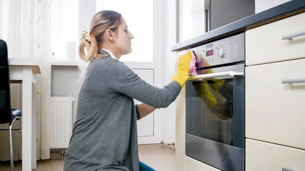 Молодая домохозяйка уборка и полировка духовки на кухне после приготовления пищи — стоковое фото