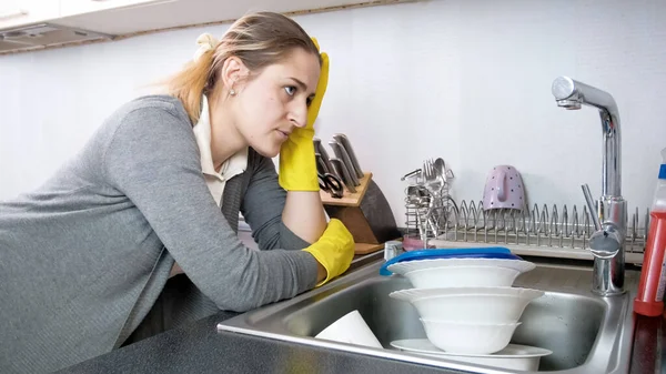 Sad and bored housewife looking on big heap of dirty dishes and cups in kitchen sink — Stock Photo, Image