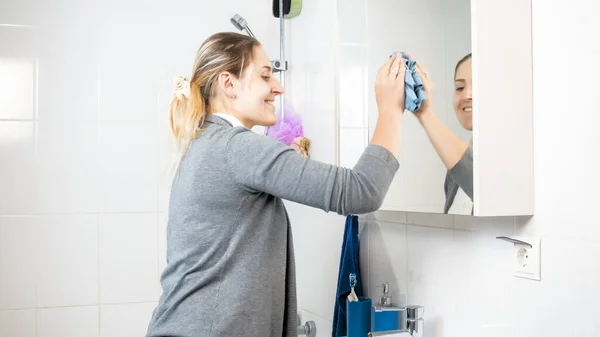 Feliz sorrindo dona de casa fazendo limpeza embanheiro e lavar espelho sujo — Fotografia de Stock