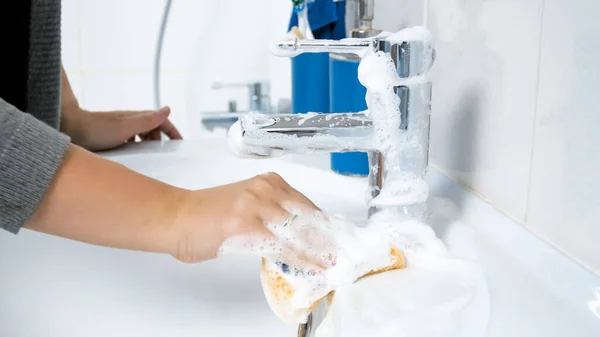Крупный план молодой женщины, стирающей раковину в ванной с пеной для моющего средства и губкой — стоковое фото