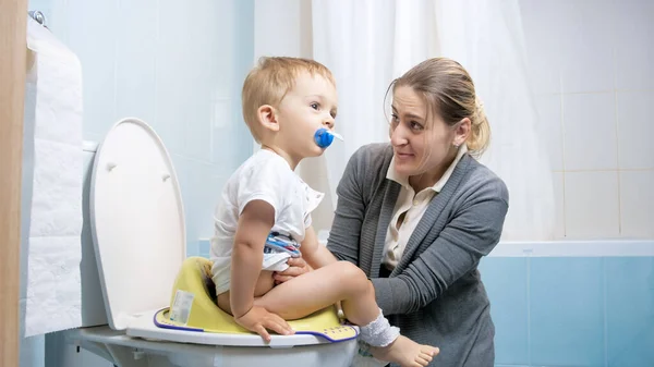 Joven madre sosteniendo a su pequeño hijo en el asiento del inodoro — Foto de Stock