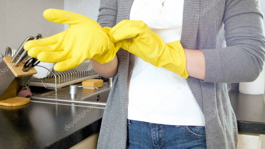 Young housewife putting on yellow protective rubber glove before doing house work