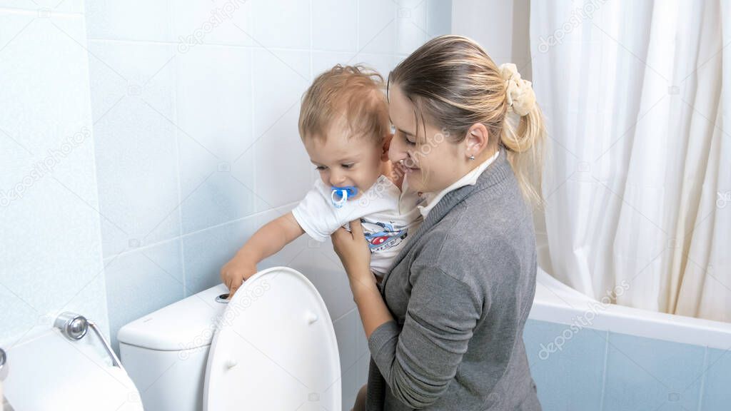 Little toddler boy flushing water in toilet with young mother