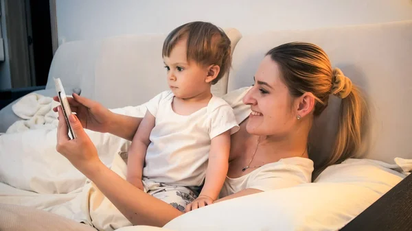 Gelukkig lachende moeder met kleine zoon met behulp van tablet computer voor het slapen gaan 's nachts — Stockfoto