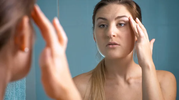 Portrait de jeune femme à la recherche de rides vieillissantes autour des yeux tout en regardant dans le miroir — Photo