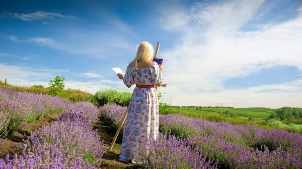 Hermosa mujer joven dibujo de la imagen en el campo de lavanda por la mañana — Foto de Stock