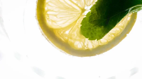 Макро фото лимонного ломтика и мятного листа, плавающего в холодном лимонаде — стоковое фото