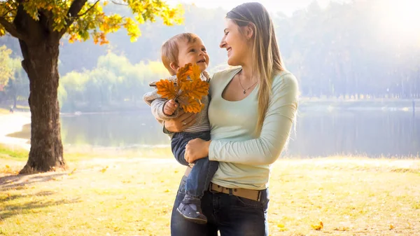 Portrait of happy smiling young mother hugging and embracing her little son at autumn park — Stock Photo, Image