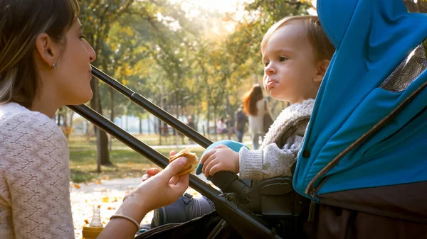 Bonito menino comendo e olhando para sua mãe no parque de outono — Fotografia de Stock