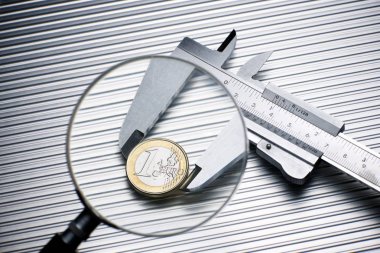 metal gauge measuring a one euro coin on a metal surface.
