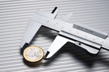 metal gauge measuring a one euro coin on a metal surface.