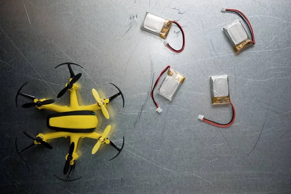 Yellow drone and batteries on a metal table.