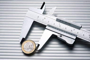 metal gauge measuring a one euro coin on a metal surface.