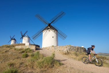 Consuegra, İspanya - 24 Haziran 2016: Don Kişot değirmenlerinin yanından geçen bisikletçi.