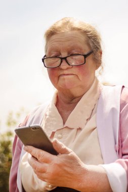 Sokakta gözlüklü yaşlı kadın cep telefonu görünüyor