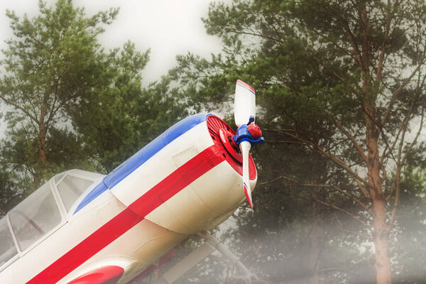 An airplane of a vintage single engine with screws flying over the trees. Close-up