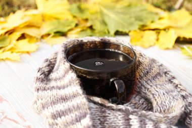 Sonbahar yaprakları, bir fincan çay, şeffaf, karanlık bir arka planda gri ahşap bir eşarp. yakın çekim