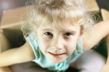 Küçük sarışın gülümser bir karton kutu içinde. Bize el gösterir. koyu arka plan. tonlama. yakın çekim.