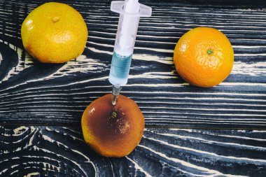 Eklenen mandarin bir şırınga. Ahşap arka plan eski stela çok karanlıktır. Şırıngada mavi sıvıdır. Gıda sektöründe kimyasal deneyler.