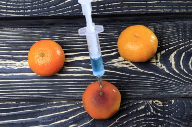 Eklenen mandarin bir şırınga. Ahşap arka plan eski stela çok karanlıktır. Şırıngada mavi sıvıdır. Gıda sektöründe kimyasal deneyler.