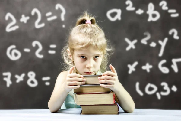 little girl blonde lies on the book. and dreams. in the background is a formula board. shallow depth of cut. have toning