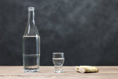 bir bardak saf alkol, bir şişe ve bir parça ekmek ve peynir ahşap arka plan üzerinde. bir cam ve üzerinde bir Kızıl Haç. çıkış içme kavramı. Orada tonlama.
