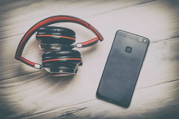 Wooden white background in the old style. headphones stacked in red. They are cordless and cell phone top view. there is toning.