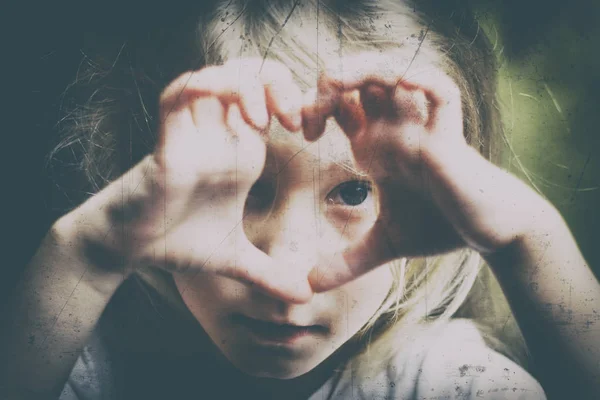 A girl with white hair makes a heart and looks into it. Concept view in childhood. there is toning — Stock Photo, Image