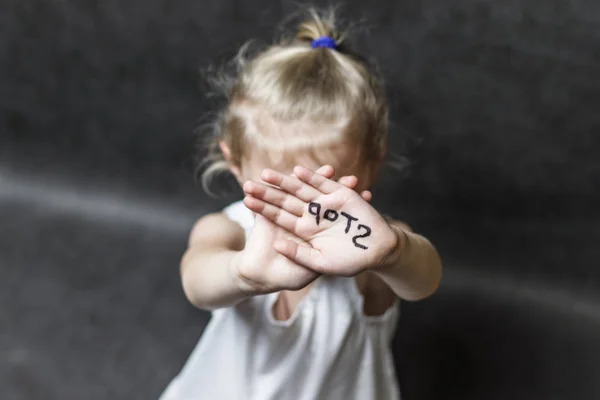 On a dark background, a child with his hands covers his face with a handwritten stop. Concept protect children from violence — Stock Photo, Image