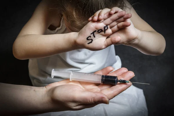 The child covers his face. on hand inscription stop. on the other hand a syringe with a dark solution for injection. The concept of anti-norcomania in adolescence — Stock Photo, Image