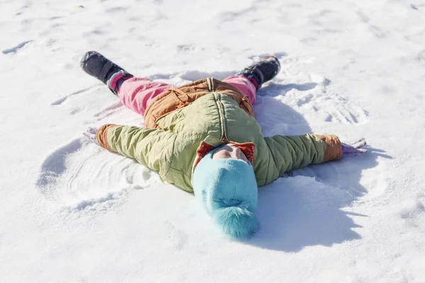 La niña dibuja en el ángel de la nieve. profundidad de campo poco profunda . —  Fotos de Stock