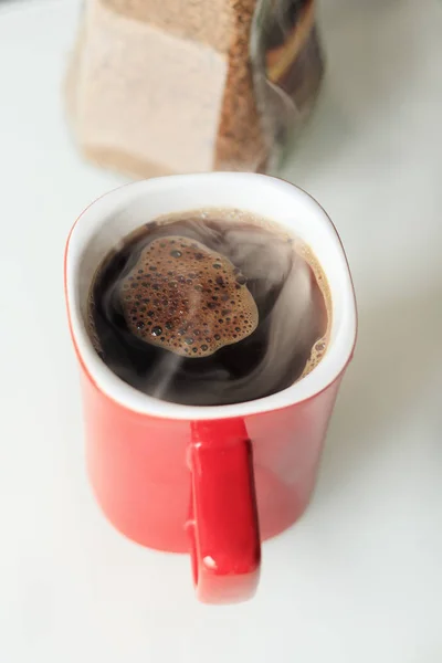 Cană roşie. Cafeaua se toarnă în ea. El este un adevărat abur. lângă borcanul de sticlă, granulele de cafea sunt deschise în el — Fotografie, imagine de stoc