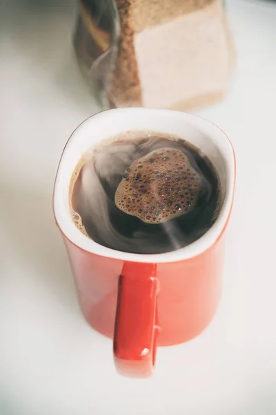 Cană roşie. Cafeaua se toarnă în ea. El este un adevărat abur. lângă borcanul de sticlă, granulele de cafea sunt deschise în el — Fotografie, imagine de stoc