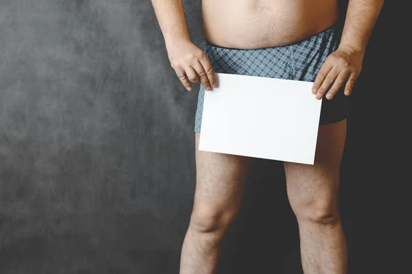 Un hombre en pantalones cortos en el fondo de la junta escolar, en sus manos tiene una hoja de papel en blanco . —  Fotos de Stock