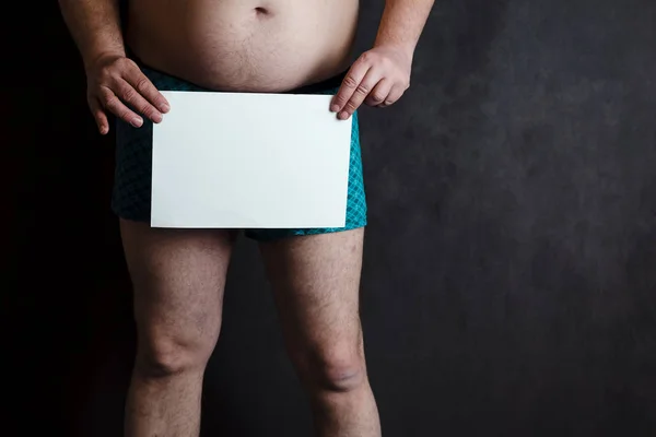 Un hombre en pantalones cortos en el fondo de la junta escolar, en sus manos tiene una hoja de papel en blanco . —  Fotos de Stock