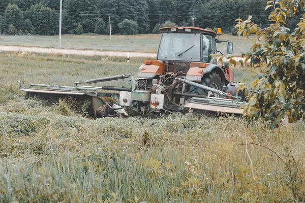 O tractor corta a relva. colheita de feno para o inverno — Fotografia de Stock