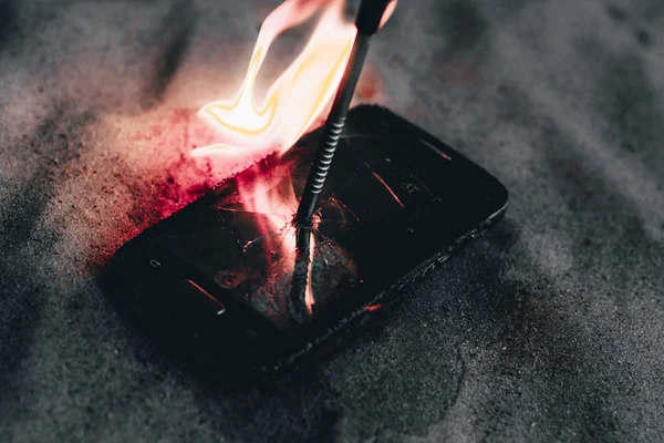 Сотовый телефон. на пляжном песке. В ней металлический гвоздь. и пылает огнем — стоковое фото