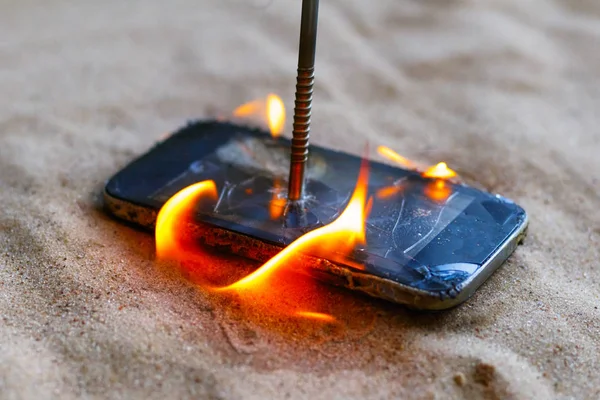 Telefono cellulare. sulla sabbia della spiaggia. Ha un chiodo di metallo dentro. brucia a fuoco aperto — Foto Stock