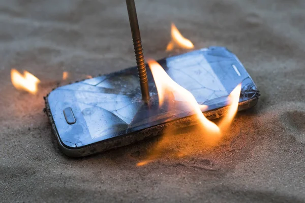 Telefono cellulare. sulla sabbia della spiaggia. Ha un chiodo di metallo dentro. brucia a fuoco aperto — Foto Stock