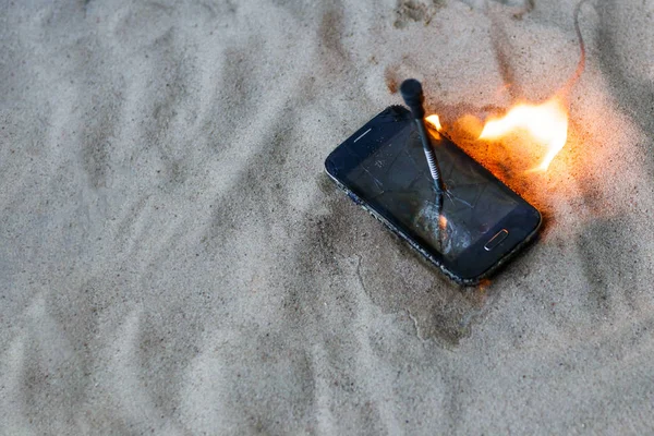 Telefono cellulare. sulla sabbia della spiaggia. Ha un chiodo di metallo dentro. brucia a fuoco aperto — Foto Stock